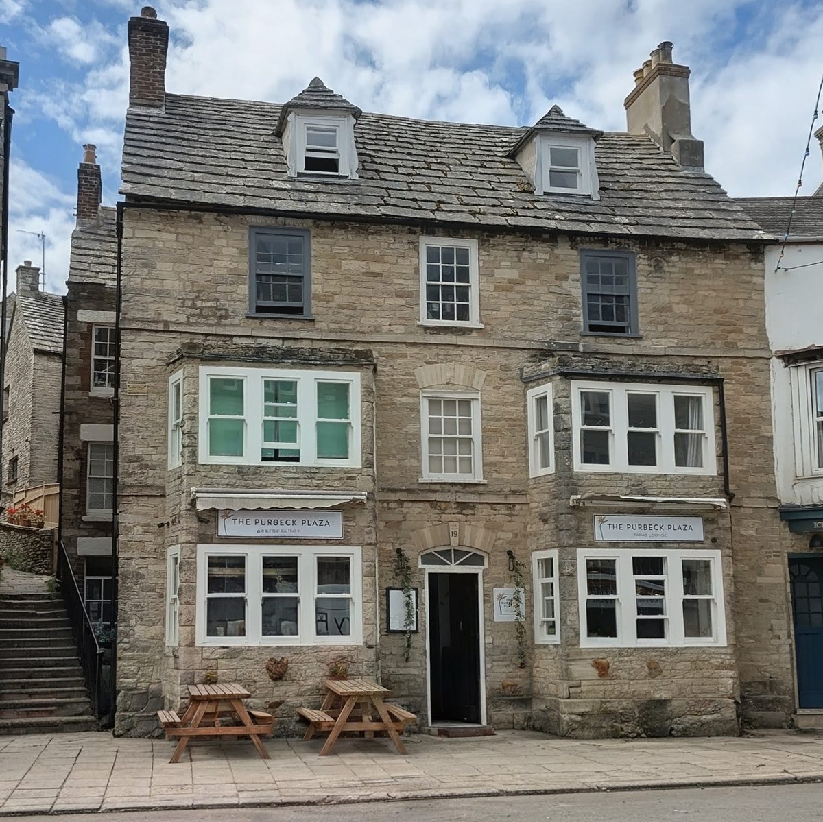 The three-storey stone building with green window frames and picnic benches outside